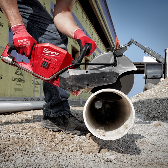 Milwaukee M18 FUEL 9-inch cordless cut-off saw cutting a concrete pipe on an outdoor jobsite, shown in use by a worker wearing gloves, with diamond blade engaged and dry cutting in progress