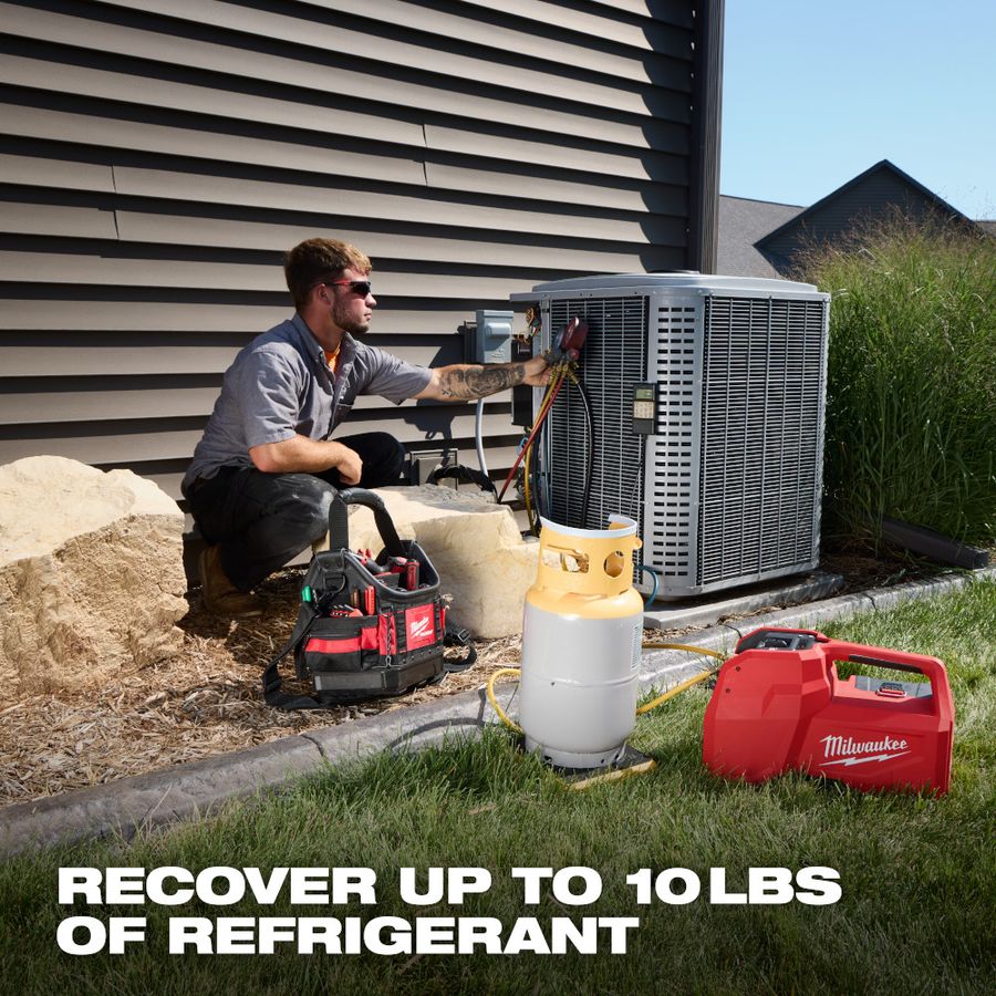 HVAC technician servicing an outdoor air conditioner while recovering refrigerant using a Milwaukee M18 brushless refrigerant recovery machine connected to a refrigerant tank and manifold gauges, demonstrating cordless recovery capability of up to 10 pounds on a residential HVAC system.