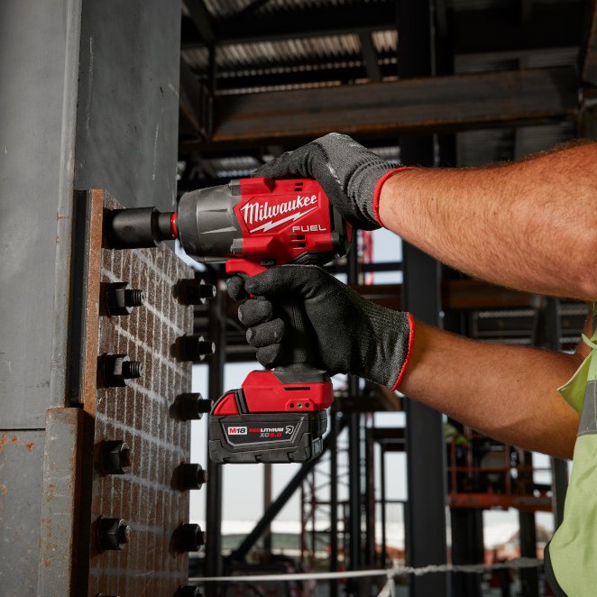 Milwaukee M18 FUEL impact wrench tightening structural bolts on a steel beam connection, shown in use with an M18 REDLITHIUM XC battery on a commercial construction site.