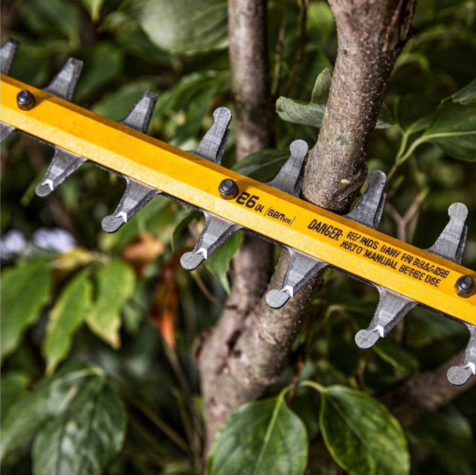 Close-up of DEWALT 60V MAX hedge trimmer 26 inch dual-action hardened steel blade cutting through small branches, showing laser-cut teeth and blade spacing in dense foliage