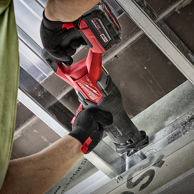 Milwaukee M18 FUEL Sawzall reciprocating saw with XC6.0 battery cutting metal framing while held with two gloved hands in a construction setting