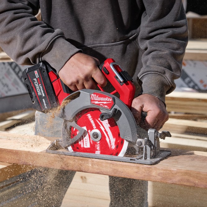 Milwaukee M18 FUEL 7-1/4 inch circular saw cutting lumber on jobsite with FORGE HD12.0 battery installed, operator hands on handles, sawdust visible during active rip cut
