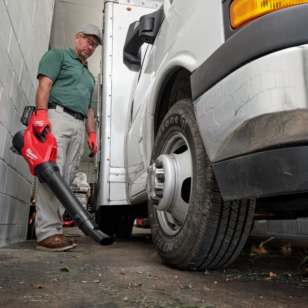Milwaukee M18 FUEL cordless blower clearing debris beside commercial truck wheel in indoor service bay