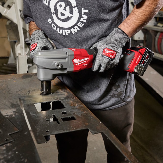 Operator using a Milwaukee M18 FUEL nibbler to cut rectangular openings in thick steel plate on a fabrication table inside a metal shop.