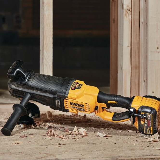 DEWALT FLEXVOLT stud and joist drill resting on subfloor at framed construction site with wood shavings around tool, side handle installed and FLEXVOLT battery attached to rear handle