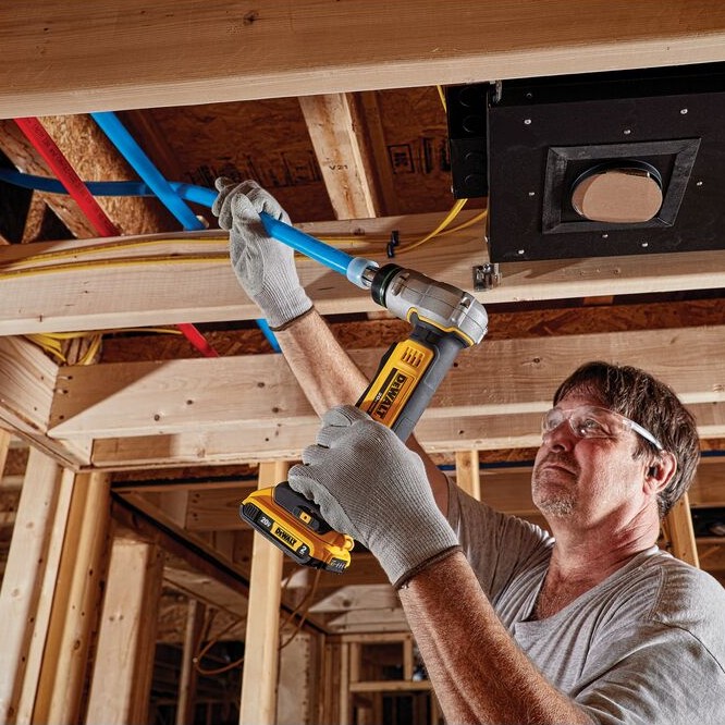 DEWALT DCE400B 20V MAX cordless PEX expander tool expanding blue PEX Type-A tubing overhead in a framed ceiling cavity, worker wearing safety glasses and gloves.