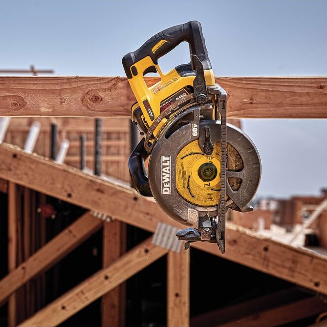 DEWALT FLEXVOLT 60V MAX rear handle worm drive style circular saw hanging from rafter hook on wood framing beam at construction site with exposed roof trusses in background