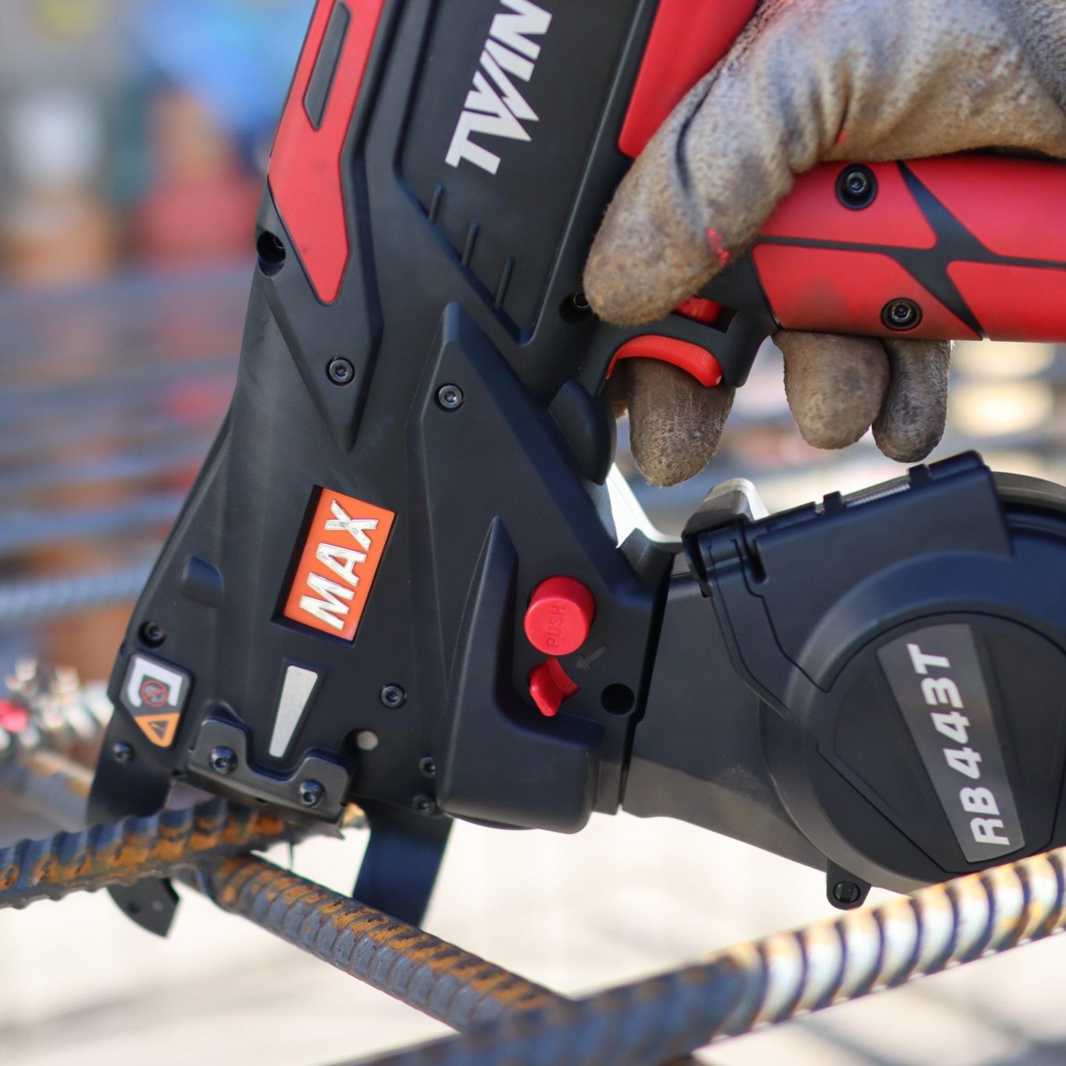 MAX RB443T cordless rebar tying tool fastening steel rebar, close-up of tool nose wrapping tie wire around intersecting reinforcing bars on a construction site