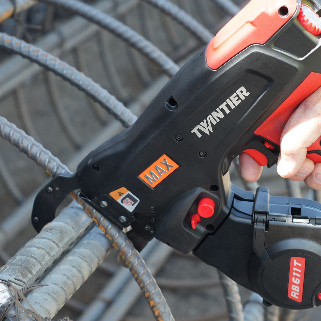MAX TwinTier cordless rebar tying tool fastening intersecting steel reinforcing bars, close-up of tool nose wrapping tie wire around rebar on a construction site