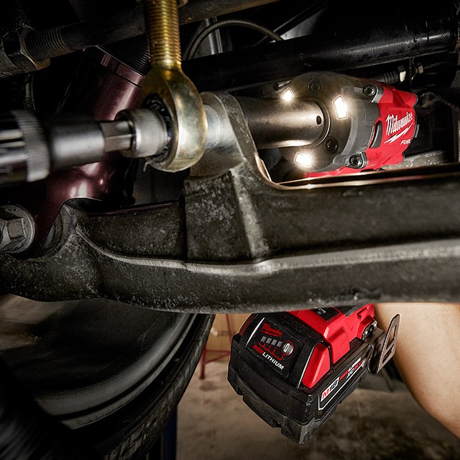 Milwaukee 2855-22R M18 FUEL 1/2" compact impact wrench with tri-LED lights illuminating suspension fastener, removing bolt in tight undercarriage space with XC5.0 battery installed