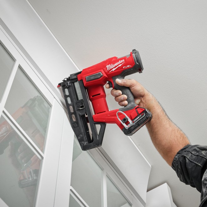 Milwaukee 3020-20 M18 FUEL 16 gauge straight finish nailer overhead application installing trim above cabinet, upward angle shot showing compact design and nose placement in tight space