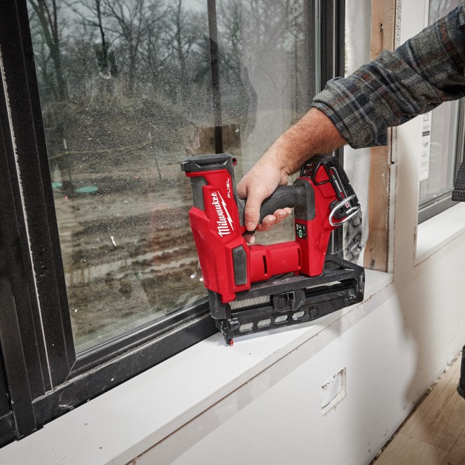 Milwaukee 3020-20 M18 FUEL 16 gauge straight finish nailer installing trim at window sill, application shot showing nailer base resting on surface with clear line of sight for precise placement