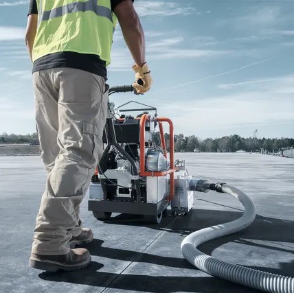 Husqvarna 966844820 SOFF-CUT 150 early entry concrete saw in use, operator cutting control joints on green concrete slab, vacuum hose attached for dust control, rear jobsite view