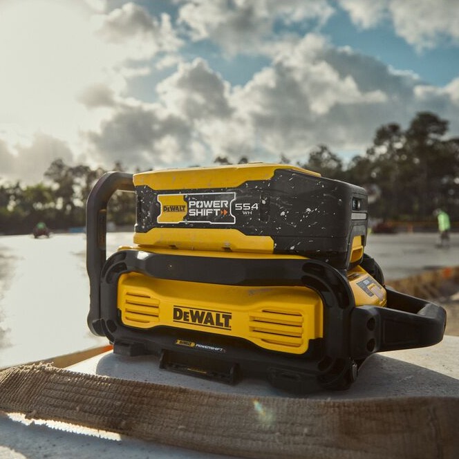 DEWALT DCBPS0554 POWERSHIFT 554Wh Battery mounted on charger on concrete jobsite, with blurred workers in background and outdoor construction setting