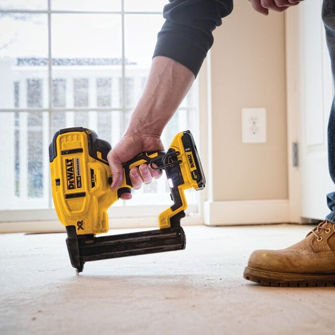 DEWALT DCN681D1 20V MAX XR 18GA narrow crown stapler in use fastening flooring underlayment, close view of cordless stapler pressed to floor with worker holding tool in residential interior setting