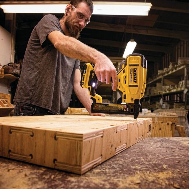 DEWALT DCN681D1 20V MAX XR 18GA narrow crown stapler in use fastening wood paneling on workbench, operator wearing safety glasses using cordless stapler in workshop setting