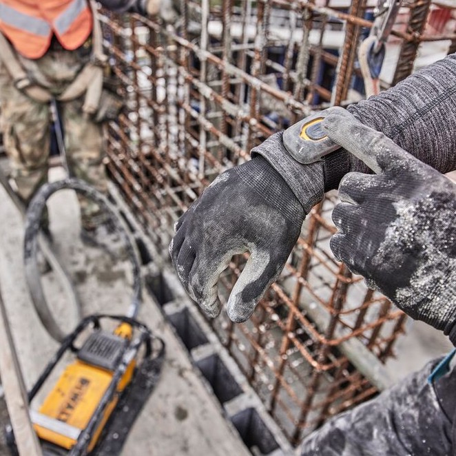 DEWALT DCPS320AG2 POWERSHIFT concrete vibrator with worker activating wireless tool control wrist remote, rebar formwork and vibrator unit visible on active jobsite