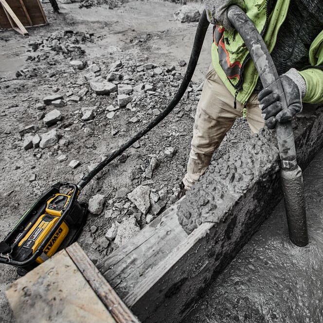 DEWALT DCPS320AG2 POWERSHIFT concrete vibrator consolidating wet concrete in formwork, showing vibrator head in pour, hose connected to unit on ground, and active jobsite conditions