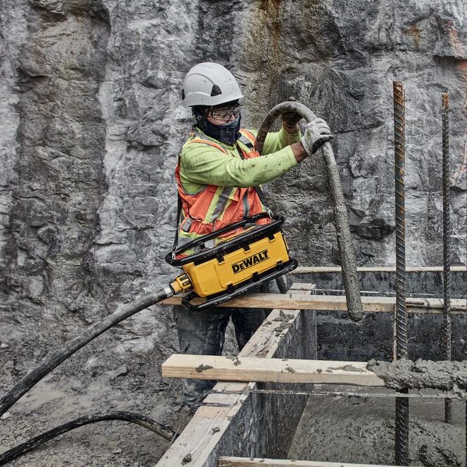DEWALT DCPS320AG2 POWERSHIFT concrete vibrator worn with shoulder strap, worker consolidating concrete in formwork with rebar and footing structure visible