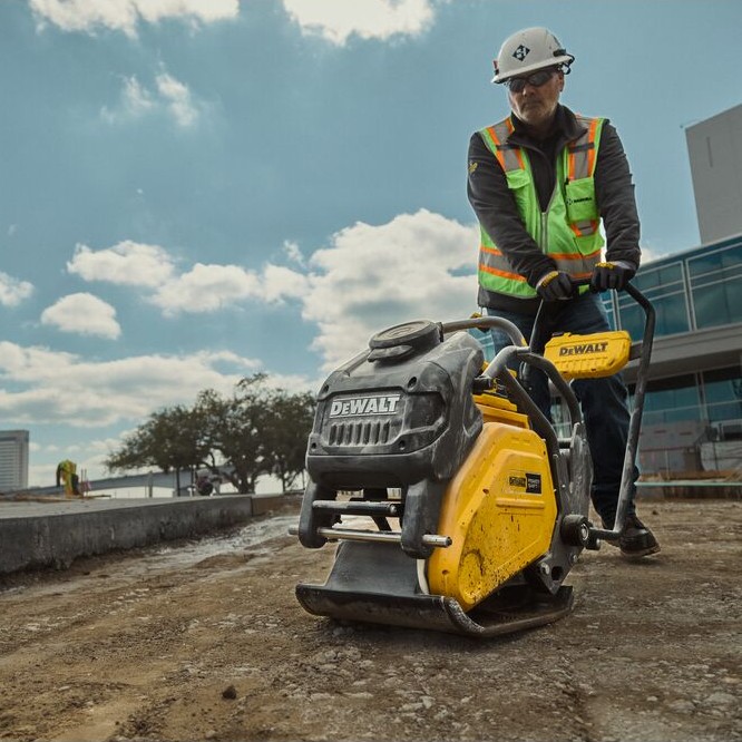 DEWALT POWERSHIFT forward plate compactor in use on construction site compacting soil, operator wearing hard hat and high-visibility vest pushing unit over prepared base