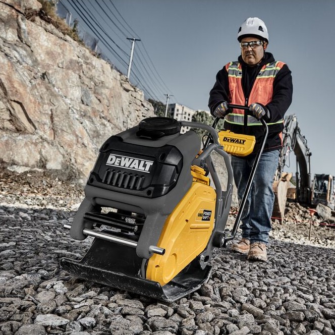 DEWALT POWERSHIFT forward plate compactor compacting gravel base on construction site, operator wearing hard hat and high-visibility vest guiding unit over crushed stone surface
