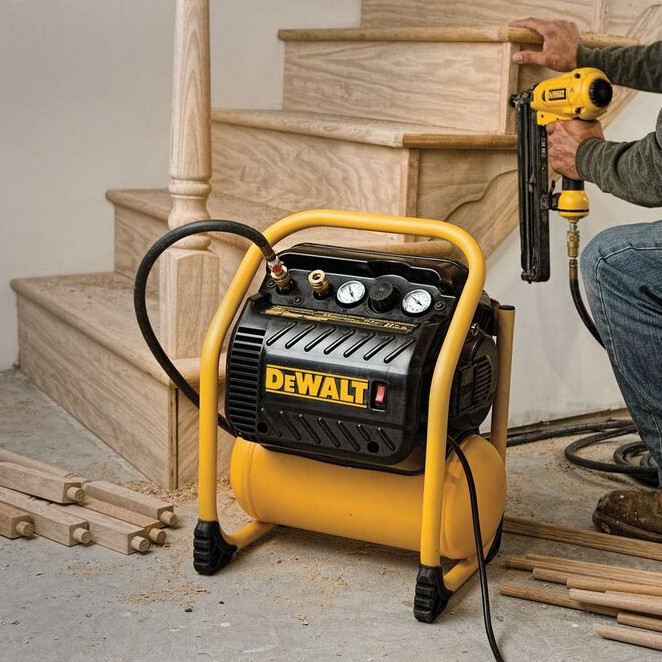 DEWALT DWFP55130 200 PSI quiet trim compressor in use powering finish nailer, jobsite setup beside wood staircase, air hose connected, trim installation application indoors