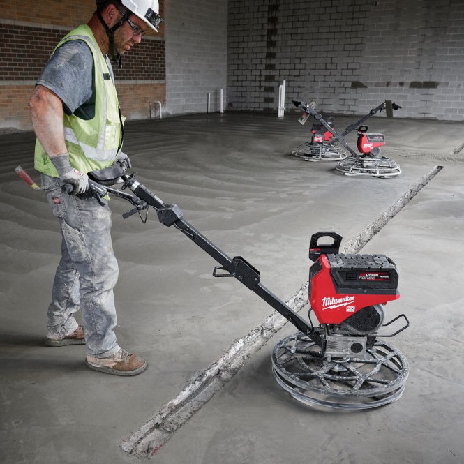 Milwaukee MXF324-2HD MX FUEL 24 inch walk behind edging trowel finishing concrete slab edge indoors with operator, additional trowels visible in background on wet concrete floor