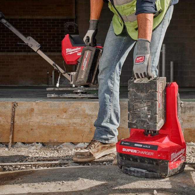 Milwaukee MXFSC MX FUEL Super Charger with REDLITHIUM battery being removed by gloved worker on jobsite, charger on ground with power cord, concrete work area and power trowel in background