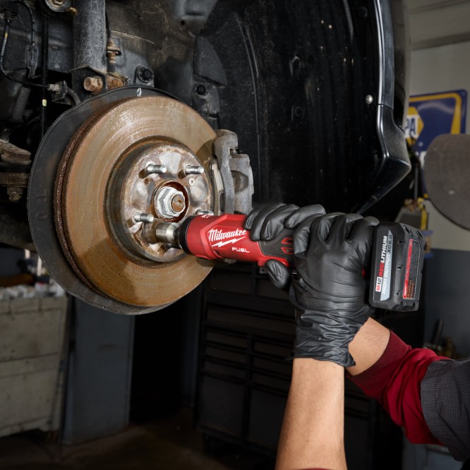 Milwaukee M12™ FUEL™ 1/4" Straight Die Grinder cleaning a wheel hub on a vehicle brake assembly, demonstrating cordless precision for automotive repair and metal surface preparation.