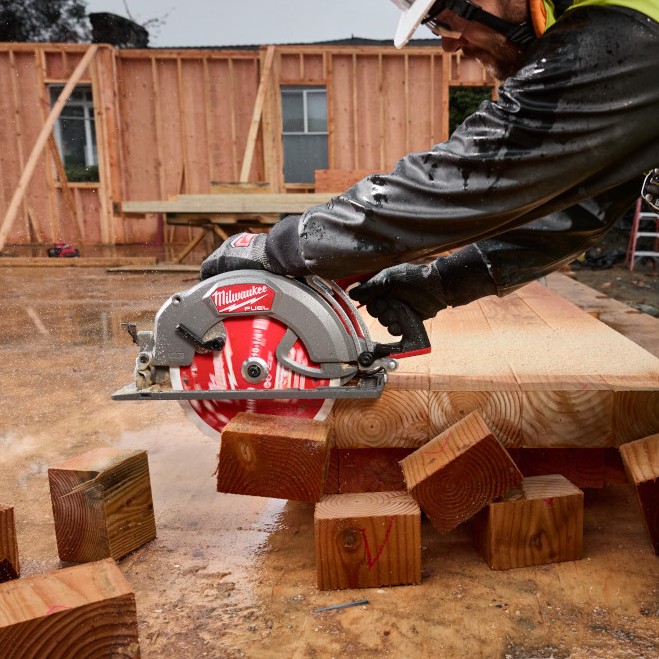 Carpenter using a Milwaukee M18 FUEL 10-1/4" rear-handle circular saw to cut multiple thick timber blocks on a wet framing jobsite.
