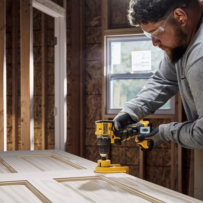 Carpenter using a DEWALT ATOMIC 20V MAX Brushless Drill/Driver to drill a door for hardware installation