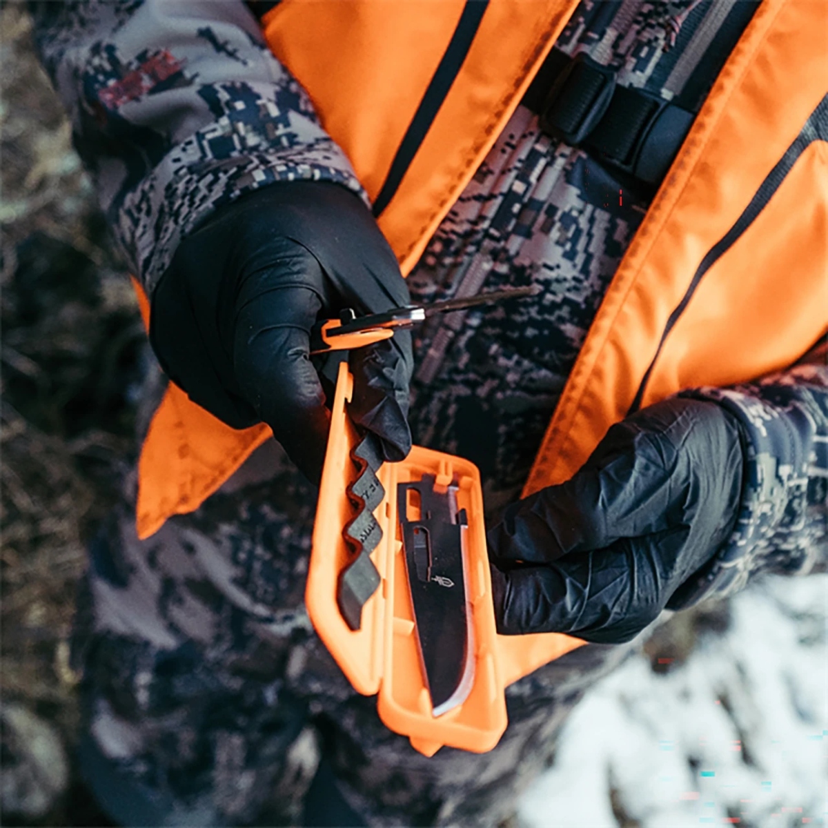 Hunter wearing gloves and an orange vest holding the GERBER Randy Newberg knife beside its open blade storage case.